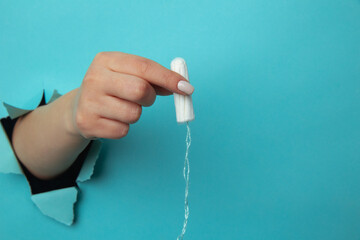 Female hand holds cotton tampon through torn paper background.