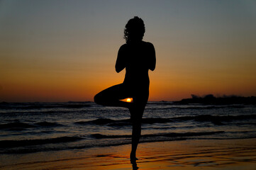 Silueta de mujer en postura de yoga en la playa al atardecer