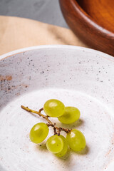 Fresh ripe white grape berries in wooden bowl with plate on linen tablecloth, stone concrete background, angle view macro