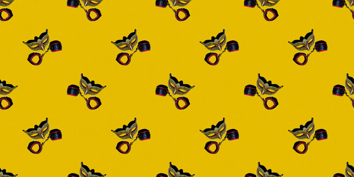 Classic Venetian theater mask with leather toy handcuffs isolated on a yellow pixel background. Seamless texture of a repeating pattern. The concept of adult Wallpaper for design.