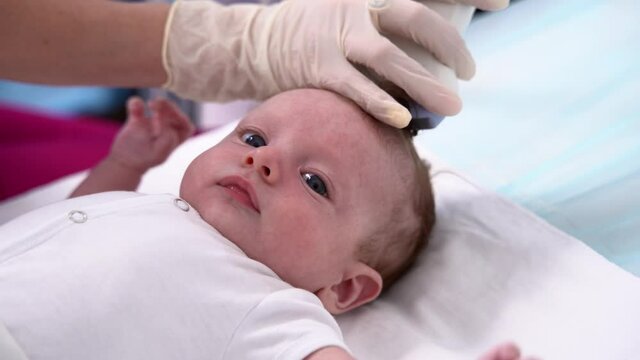 A female doctor conducts an ultrasound examination of the head and brain of a newborn baby using modern medical equipment in a clinic. Pediatrics and control of the development of the child's body.