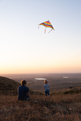 dad and toddler boy son fly a kite at sunset.