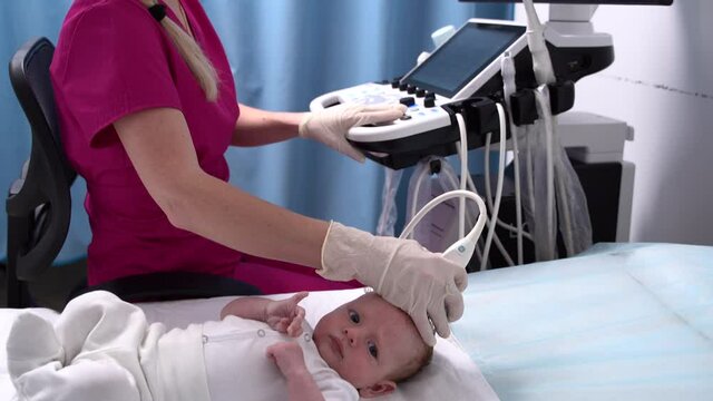 A female doctor conducts an ultrasound examination of the head and brain of a newborn baby using modern medical equipment in a clinic. Pediatrics and control of the development of the child's body.
