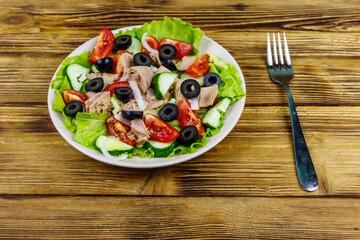 Tasty tuna salad with lettuce, black olives and fresh vegetables on wooden table