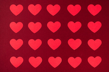Little hearts made from red paper covering the frame as a symmetrical pattern on a dark red background. Valentines Day background.