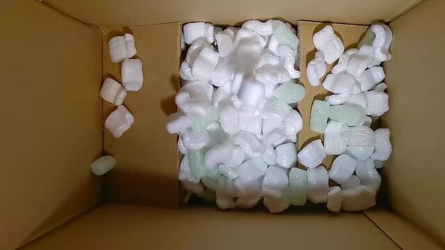 Filling an empty box green foam rubber and white styrofoam chips filler. Filler falls into a cardboard box for packing, slow motion