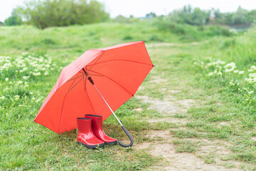 Romantic red boots and an umbrella stand on the green grass in the middle of the spring day