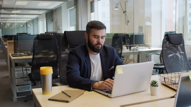 Zoom-in medium shot of serious mixed race business man working on laptop in empty open space office