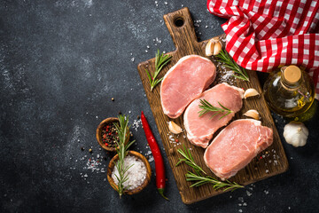 Pork meat. Fresh pork steaks on cutting board with ingredients for cooking. Top view at black stone...