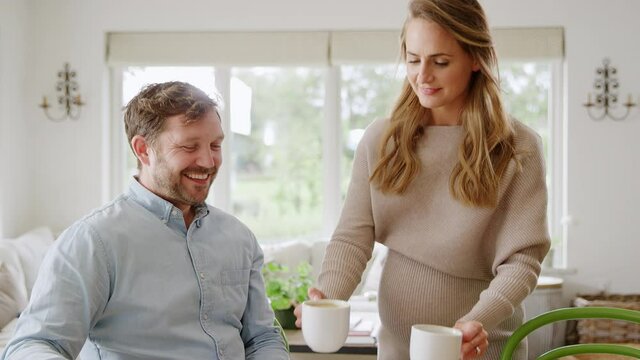 Pregnant woman bringing man cup of coffee as they review domestic finances together - shot in slow motion