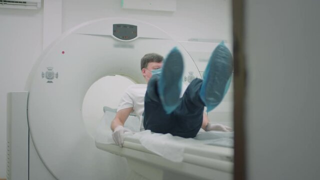 A patient in a protective medical mask lies in a modern computed tomography apparatus. The doctor analyzes the lungs on a CT scanner. The danger of covid or coronavirus. Human lung scans