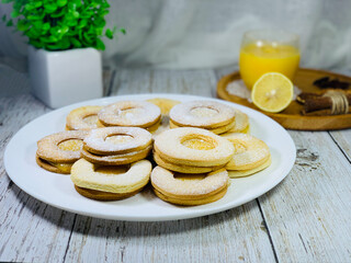 Cookies sprinkled with icing sugar on a white plate. Round biscuits with lemon filling. Lemon and honey on a wooden plate, background.