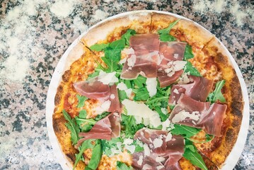Pizza from the oven. Oven-baked pizza with Italian ham and arugula close up