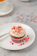 Red velvet cupcakes with cream cheese icing are decorated for Valentine's Day on a white plate on a gray background. Copy space.