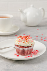 Red velvet cupcakes with cream cheese icing are decorated for Valentine's Day on a white plate on a gray background. Copy space.