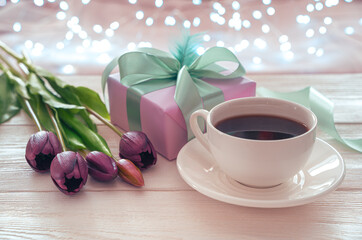 Festive background with a cup of coffee, flowers and gift packaging on the background of a burning garland. Side view. The concept of holiday backgrounds.