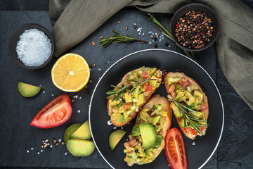 Avocado on toast, tomatoes and lemon on a black background. Top view, with space to copy. The concept of healthy eating.