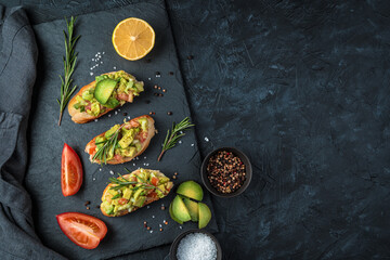 A culinary backdrop with avocado sandwiches and fresh vegetables on a black concrete table. Top view, with space to copy. The concept of proper nutrition.