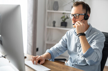 A confident young man with a headset talking online via video connection on the trendy PC. A...