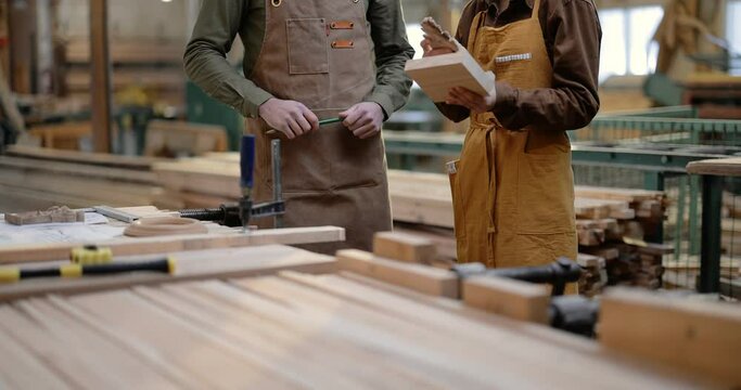 Two carpentry workers discuss woodwork at the manufacturing. Designing woodwork or supervising production. Tilt up camera movement