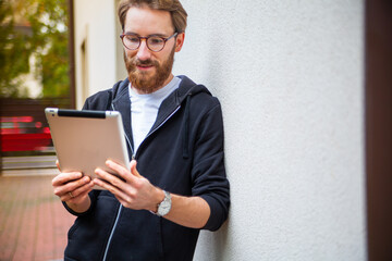 Man smiling while using a tablet outdoor, outside the house.