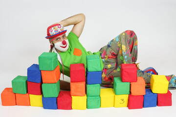 The clown is lying on the floor behind colorful cubes. Isolated on white