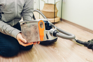 Woman holding dust filter of vacuum cleaner at home. Hoover container full of dirt and garbage....