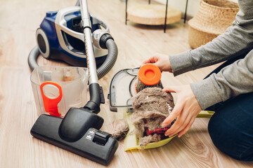 Housewife removes garbage and cat's hair from dust filter of vacuum cleaner at home. Hoover...