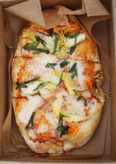 Top view on delicious Italian gourmet artichoke and mozzarella cheese pizza under tomato sauce in a cardboard box.  Lunch and street food concept. 