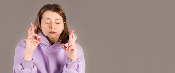 Young female student keeping her fingers crossed and eyes closed to make a desired wish