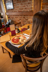 Pizza quattro stagioni with egg served in the restaurant. Woman sitting alone eating pizza in the restaurant