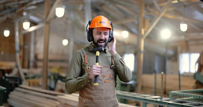 Joyful carpentry worker in safety hard hat having a break, singing and dancing at the manufacturing. Employee having fun at the factory