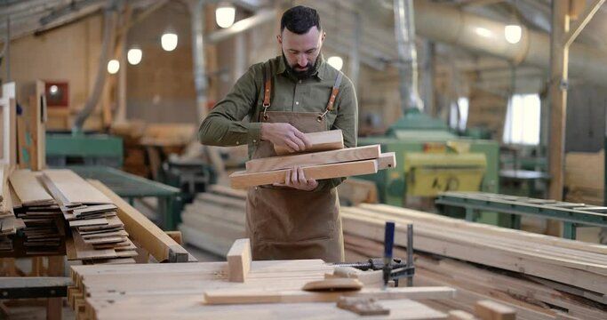 Carpentry worker carrying planks for some woodwork at the manufacturing. Handsome man working with wood at the joinery