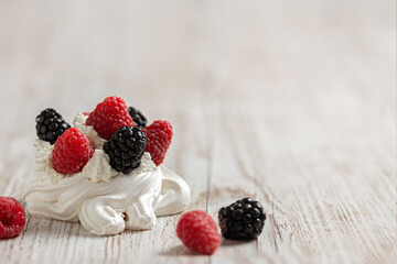 Homemade delicious Pavlova meringue cake with fresh raspberries and blackberries on a wooden background. Close-up. Copy space.