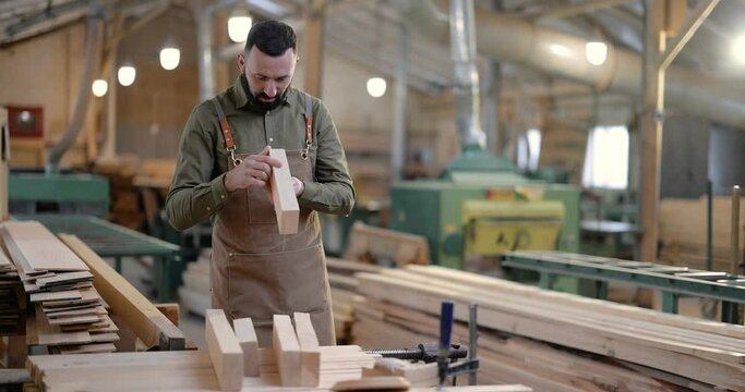 Carpenter looking on planks for some woodwork at the manufacturing. Handsome man working with wood at the joinery