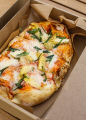 Top view on delicious Italian gourmet artichoke and mozzarella cheese pizza under tomato sauce in a cardboard box.  Lunch and street food concept. 