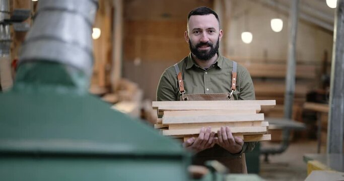 Portrait of a carpentry worker carrying planks for some woodwork at the manufacturing. Handsome craftsman working at the joinery