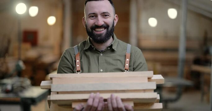 Portrait of a carpentry worker carrying planks for some woodwork at the manufacturing. Handsome craftsman working at the joinery
