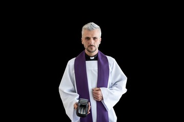Handsome catholic priest holding credit card terminal. Church and money. Isolated on black...