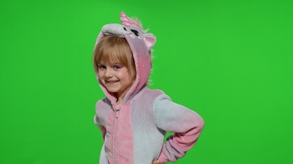 Young little blonde child 5-6 years old smiling, dancing, celebrating, making faces in unicorn costume on chroma key green background. Portrait of kid girl animator in unicorn pajamas