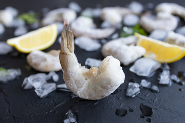 Frozen king shrimp in blurred background with ice and lemon. Delicious prawn without head for meal preparation. Enjoy natural seafood with low fat and high protein. Soft focus on foreground. Closeup.