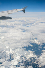 Fototapeta premium View from airborne airplane window at cloudy sky and Alps mountains with snow covered peaks from high altitude.
