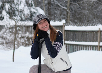 girl with a beautiful smile stands with a shovel on a winter day.