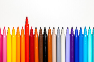 Set of markers placed in line, one red marker standing out on a white background. Focus on the foreground.