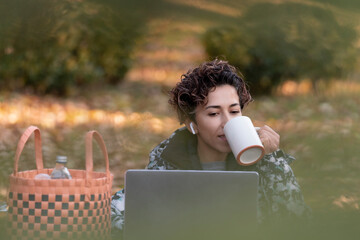 Freelance woman drinking coffee is working with laptop in the park. working outside