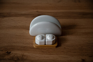 White porcelain round napkin holder and white pepper shaker and salty bowl on a wooden stand