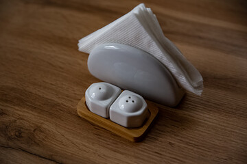 White porcelain round napkin holder and white pepper shaker and salty bowl on a wooden stand