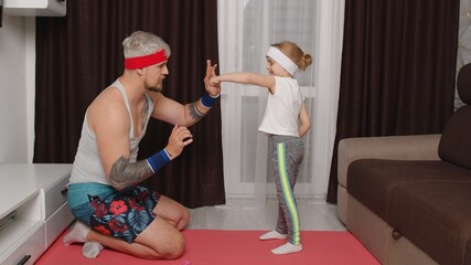 Retro style athletic man coach working out with child kid girl. Gray-haired bearded sportsman guy trainer father doing boxing exercises with daughter at home on mat. Indoors family sport workout