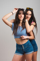 Young twin sisters. Pretty teen twins wearing striped t-shirts and jean shorts on light grey background
