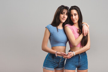 Young twin sisters. Pretty teen twins wearing striped t-shirts and jean shorts on light grey background